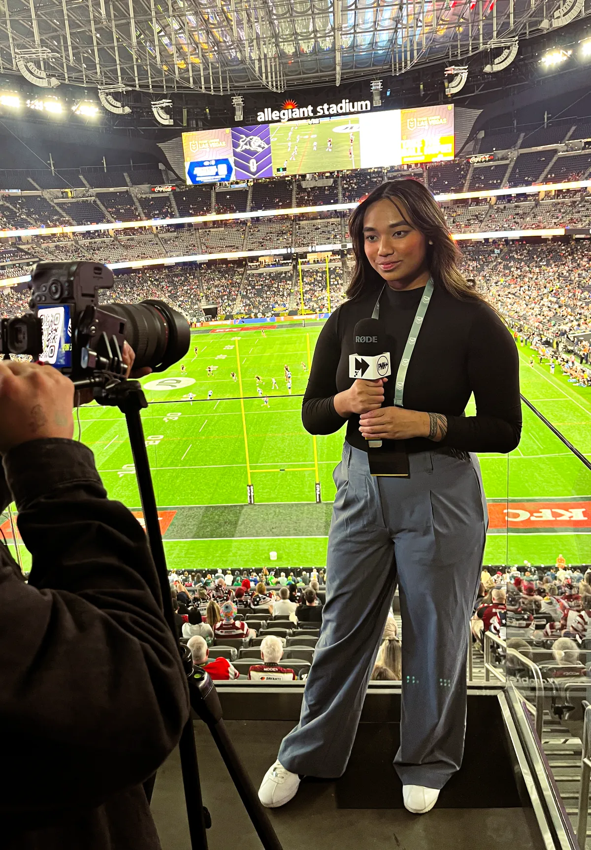 PMN+ reporter Keilani Mayo presenting to camera with a PMN+ microphone above the field at Allegiant Stadium, Las Vegas