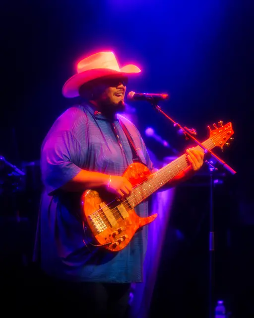 Bassist in a cowboy hat playing under purple lights