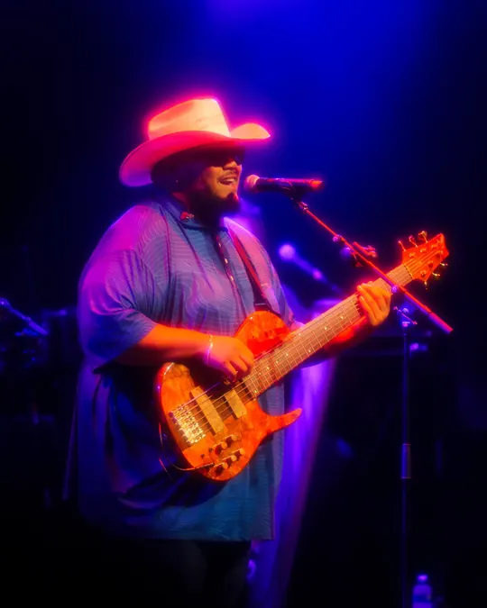 Bassist in a cowboy hat playing under purple lights
