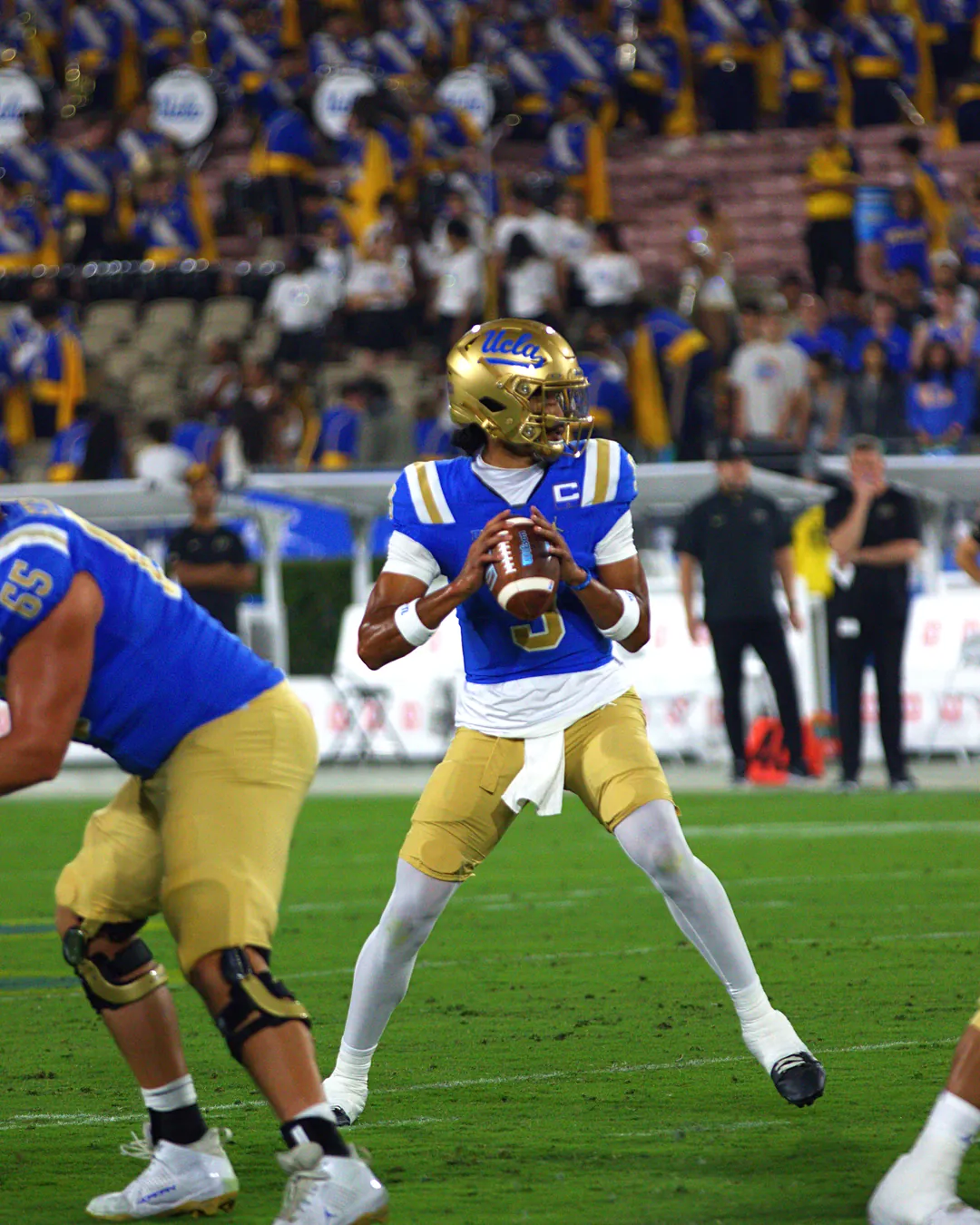 UCLA quarterback dropping back to pass in front of a packed student section at the Rose Bowl
